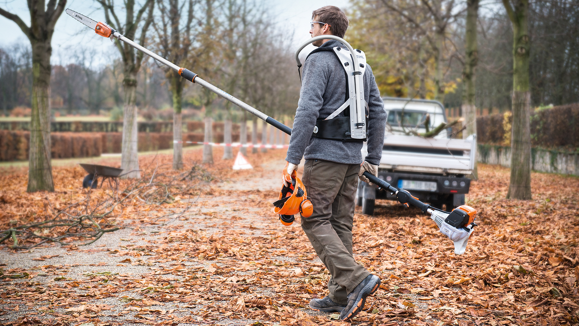 Mand med STIHL HT 133 benzinbeskærer og arbejdskøretøj i parken i efteråret