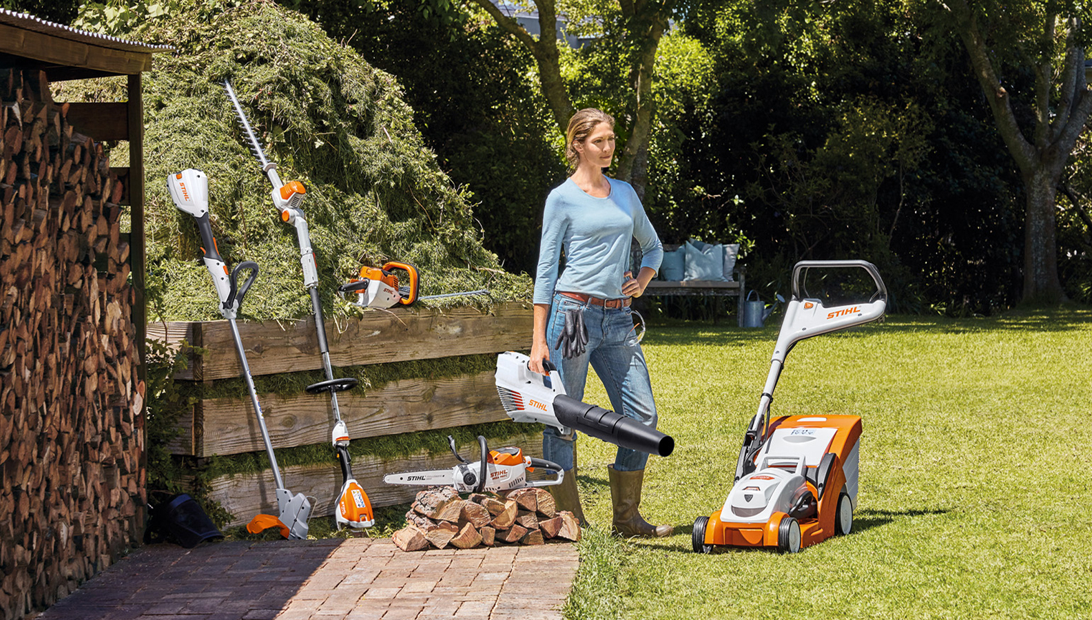 Kvinde, der står i haven med et udvalg af batteriprodukter fra STIHL