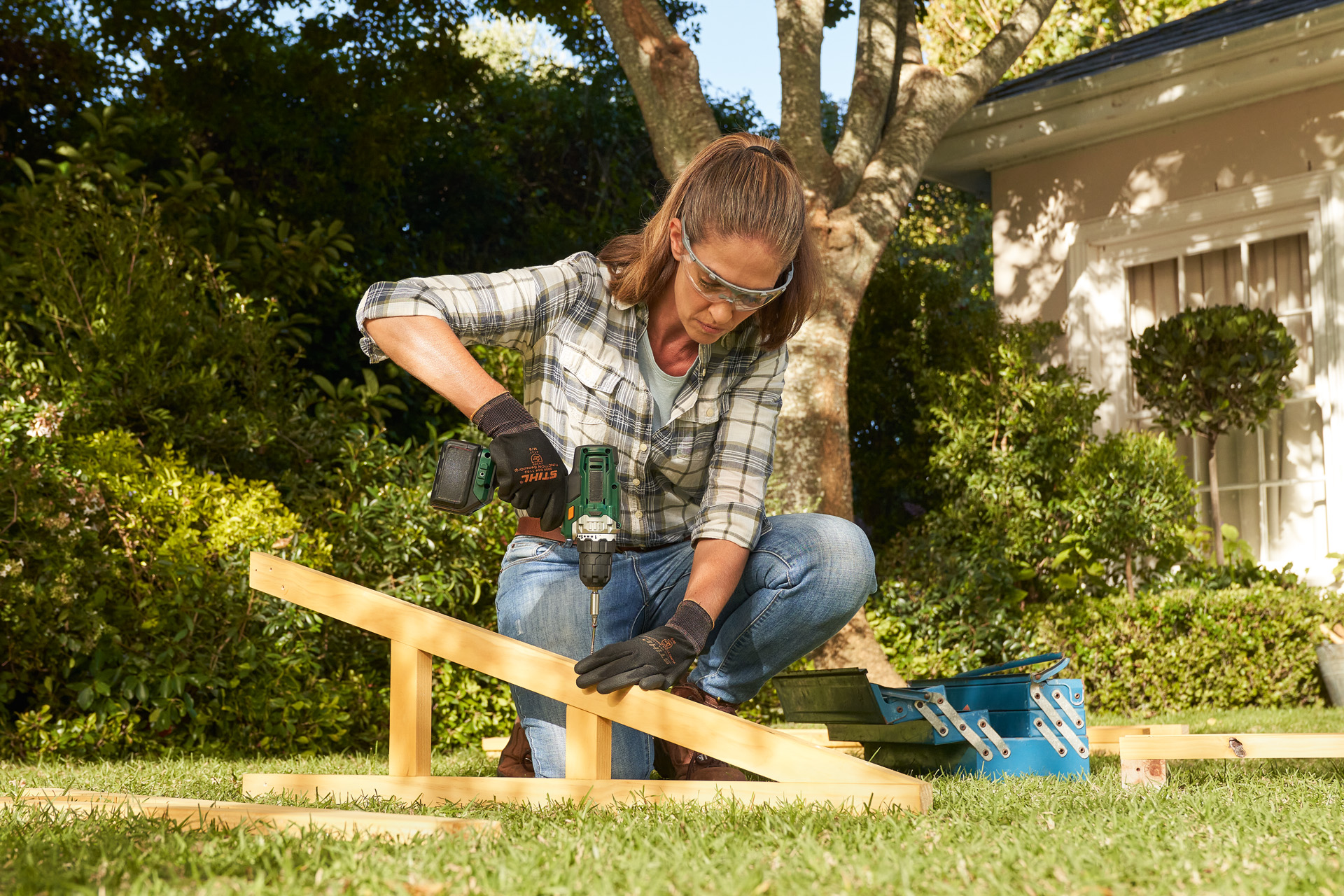 En person med STIHL beskyttelseshandsker bruger en batteriboremaskine på en træbjælke