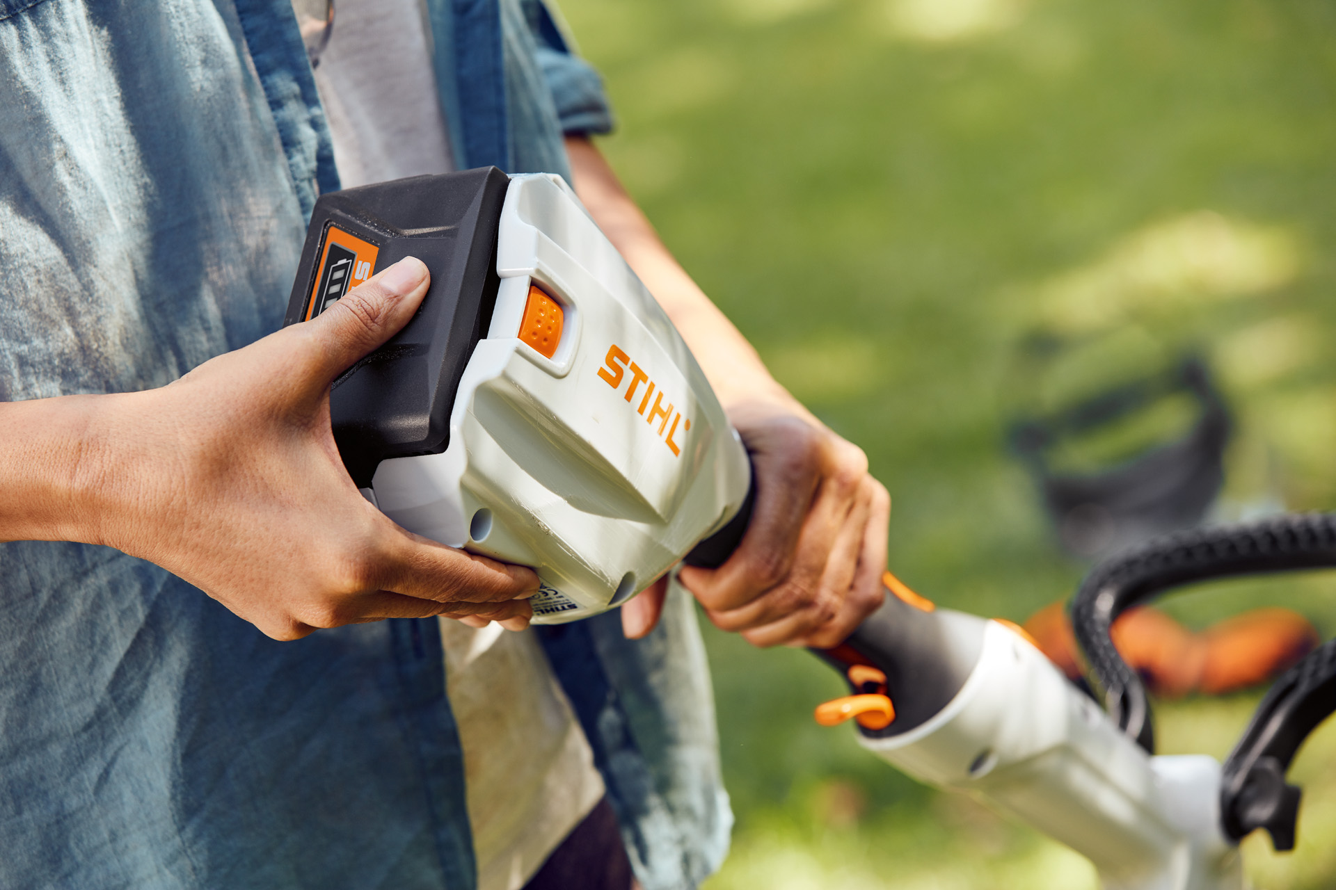 En person holder den batteridrevne STIHL trimmer FSA 56 i hånden og stryger hen over batteriet.