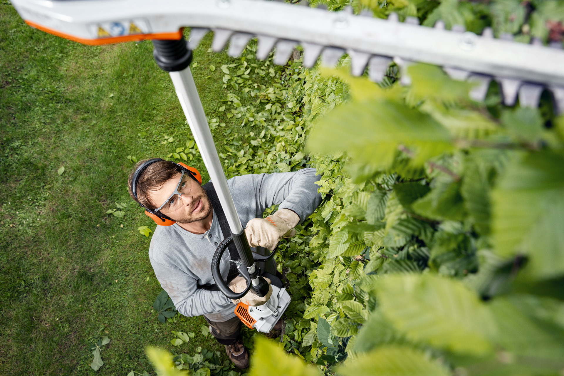 En mand med beskyttelsestøj klipper en hæk lodret i siderne med en STIHL stanghækkeklipper HL 94