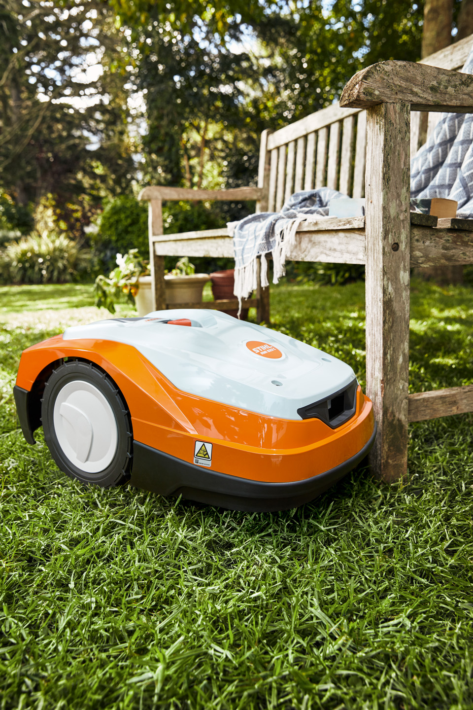 En STIHL iMOW® RM 522 robotplæneklipper på en grøn græsplæne ved siden af en bænk