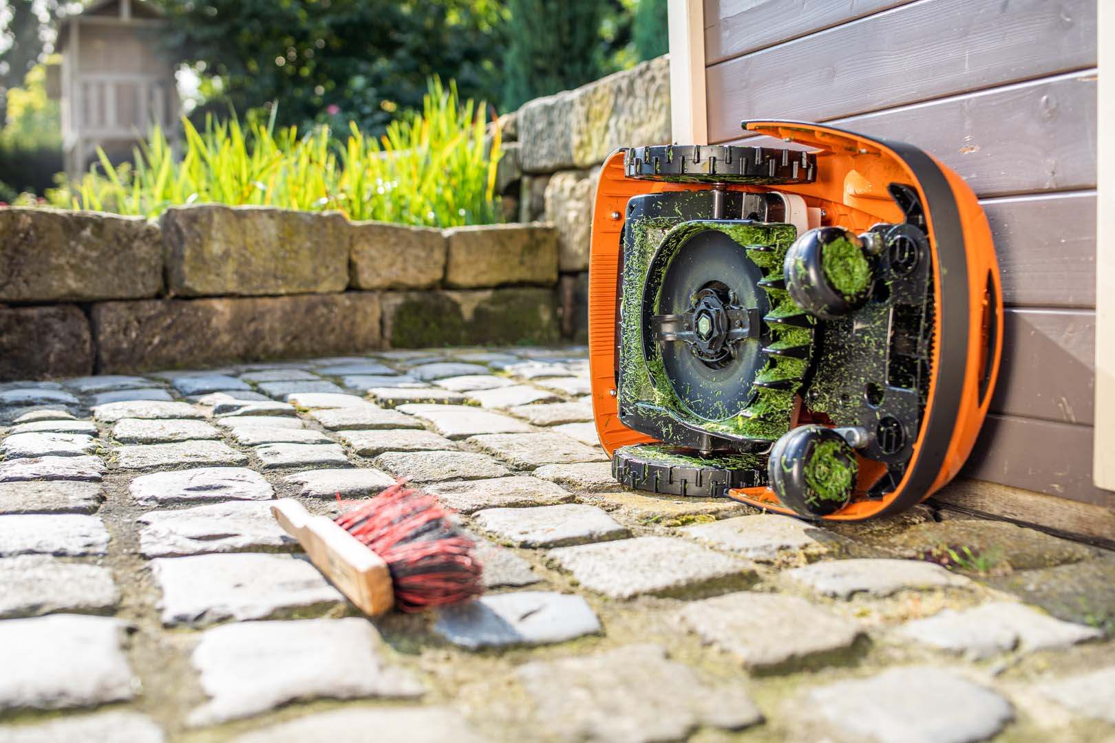 En STIHL iMOW® robotplæneklipper vendt om på siden ligger klar til rengøring med en børste på jorden i nærheden