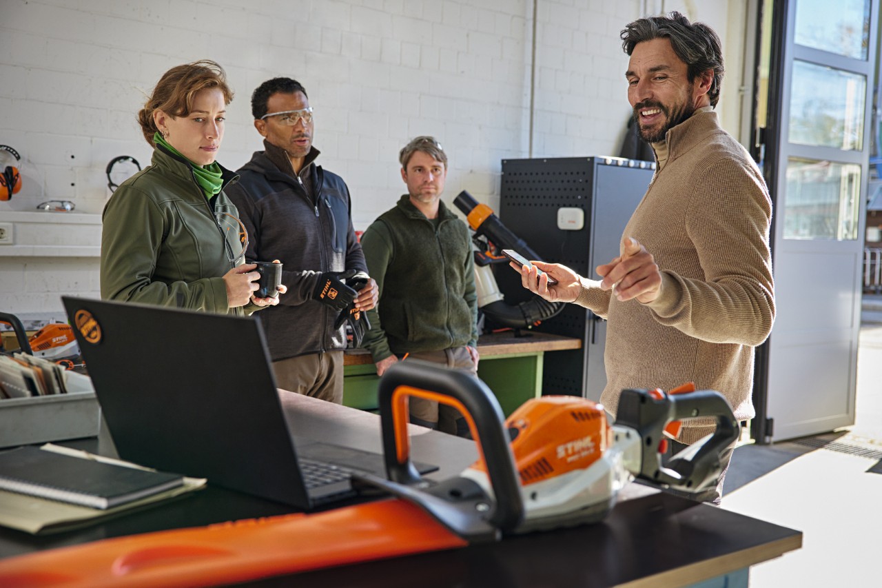 Il team di giardinieri paesaggisti discute il proprio lavoro in un magazzino utilizzando l'app STIHL connected sullo smartphone.