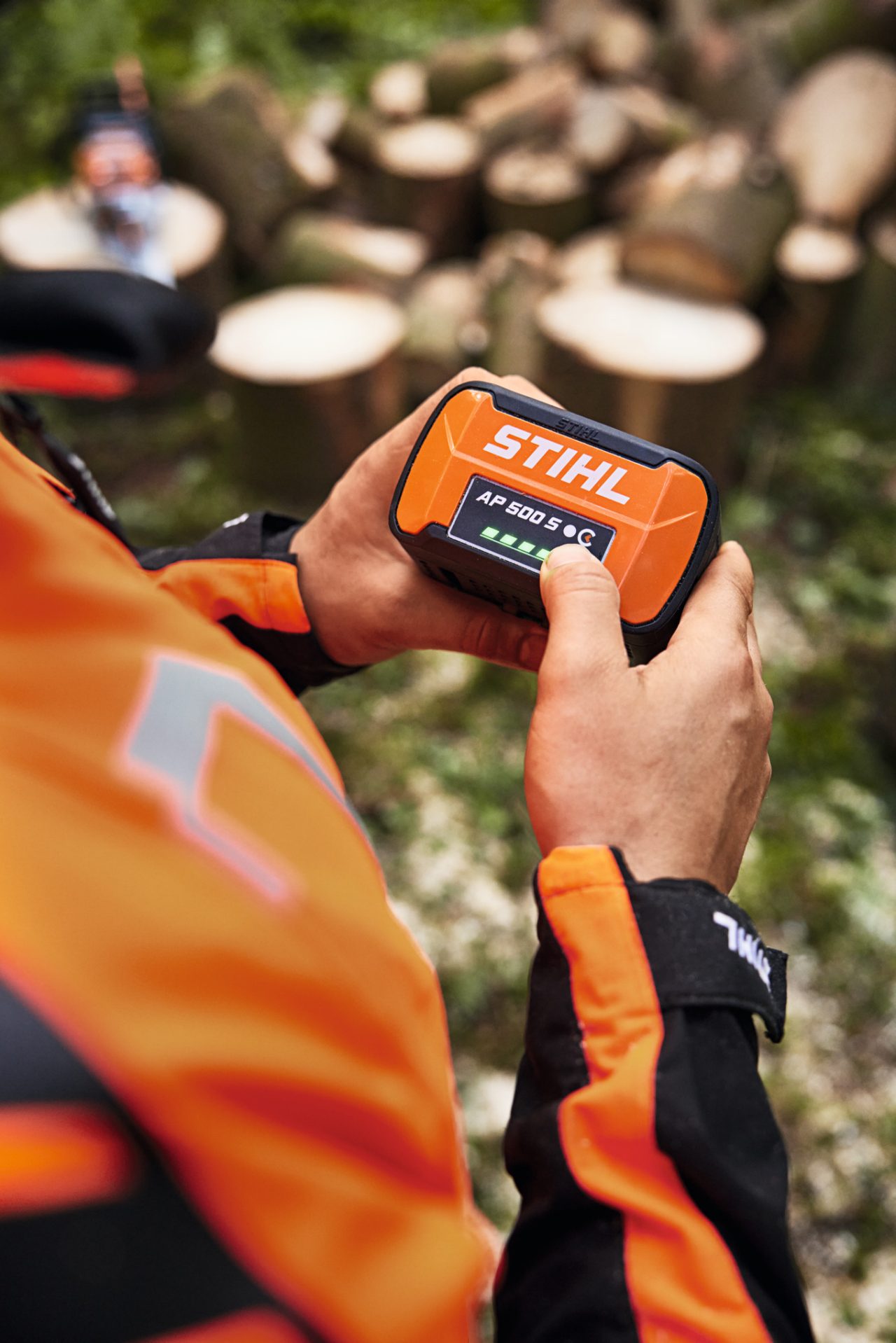 En person holder et STIHL AP 500 S-batteri i hænderne. Opladningstilstandsindikatorens lysdioder lyser grønt. 