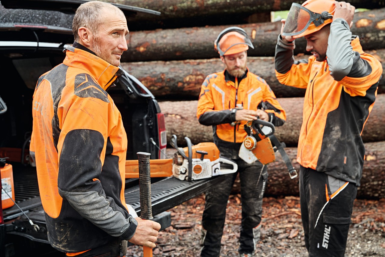Tre mænd iført personligt beskyttelsesudstyr fra STIHL ved siden af et køretøj med åben bagagerumsklap