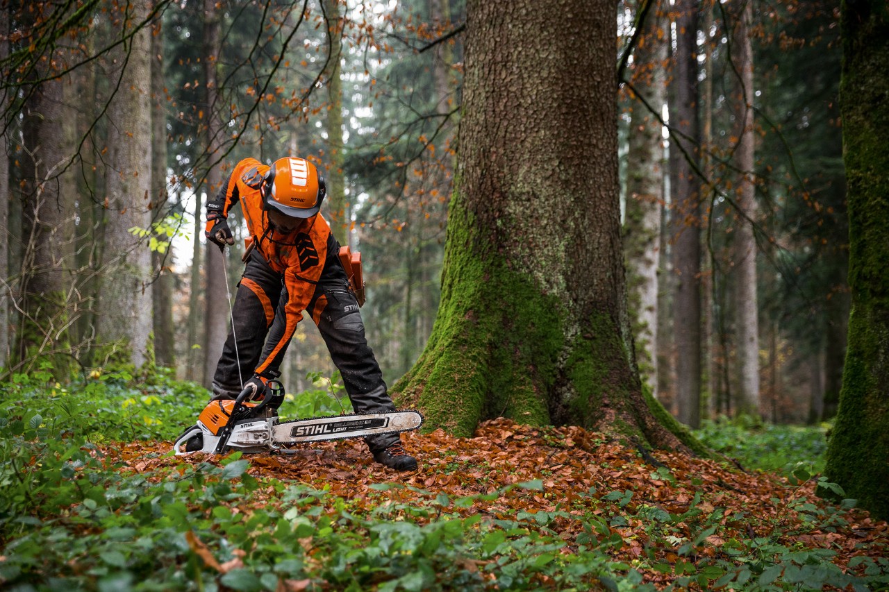 En man i skyddskläder startar STIHL bensinmotorsåg MS 500i på marken i en lövskog