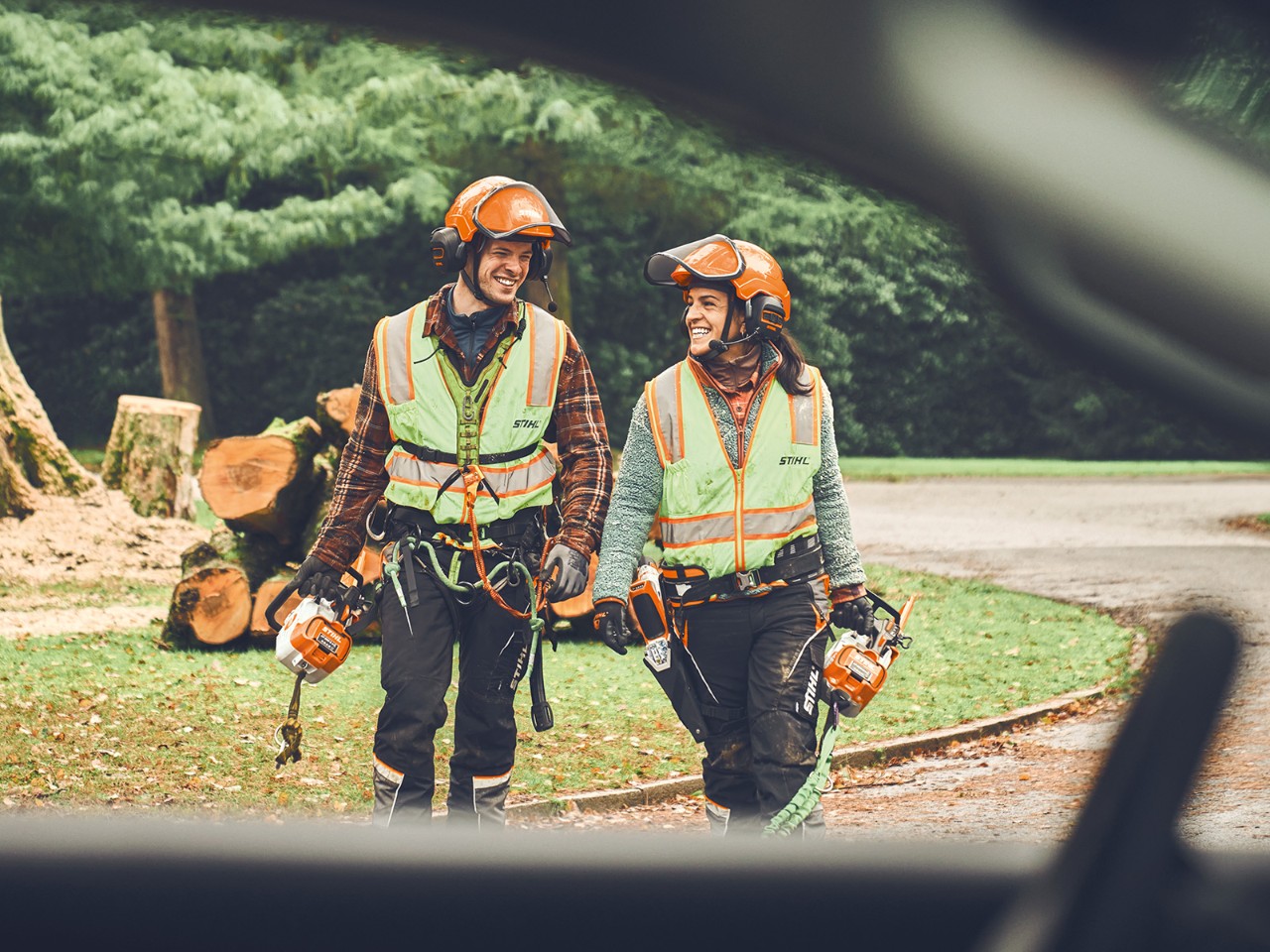En mand og en kvinde med STIHL akku motorsave og en STIHL akku trætrimmer går smilende hen mod en bil
