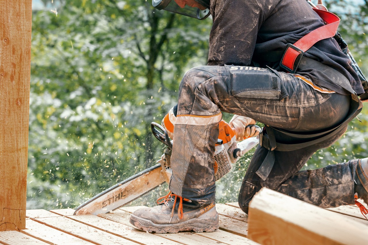 En person iført arbejdsstøvler og STIHL Advance X-Light-bukser saver en kant af en træplatform med en STIHL-motorsav