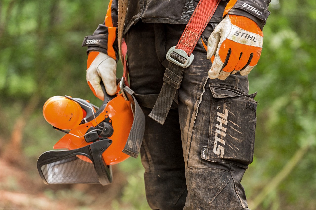 En person iført STIHL arbejdsbukser og handsker holder en hjelm 