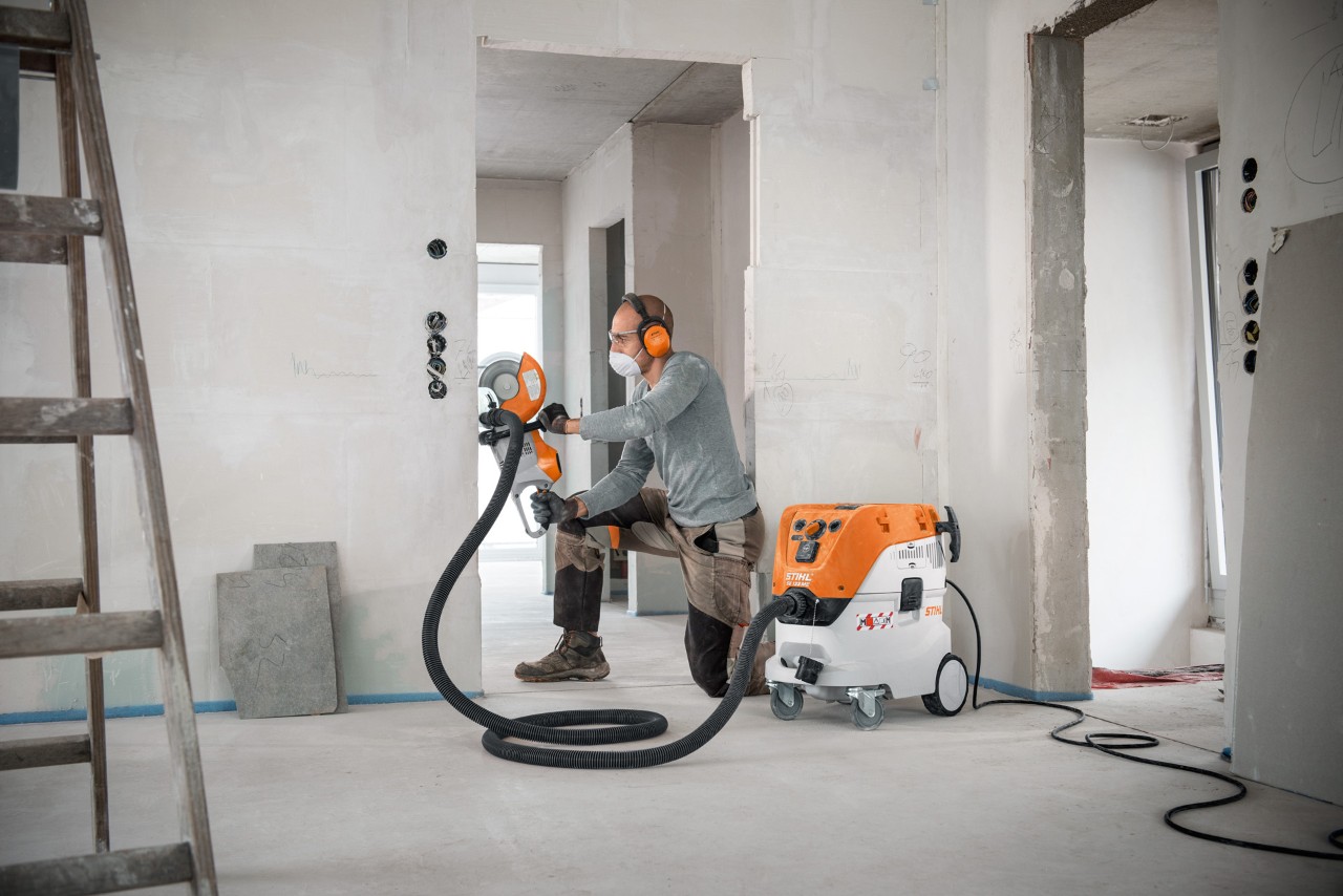 En mand bruger en STIHL SE 133 ME våd-/tørstøvsuger, mens han arbejder med en STIHL TSA 230 skæremaskine