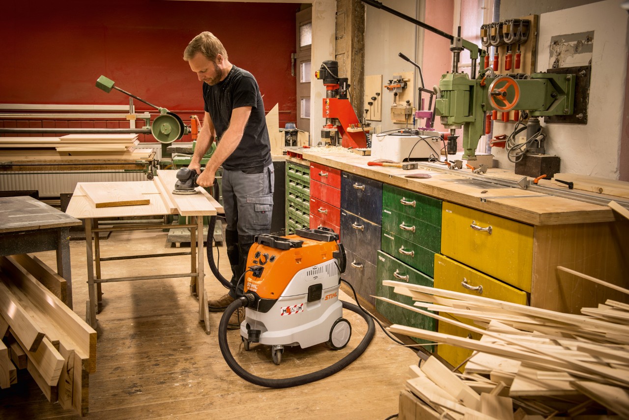 Mand, der bruger en STIHL SE 133 ME våd-/tørstøvsuger på et værksted, mens han arbejder med træplanker