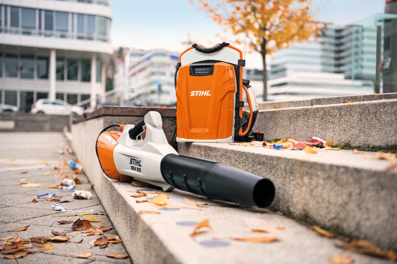 Den batteridrevne løvblæser STIHL BGA 100 og det professionelle rygsækbatteri STIHL AR 3000 L placeret på en stentrappe med nogle blade