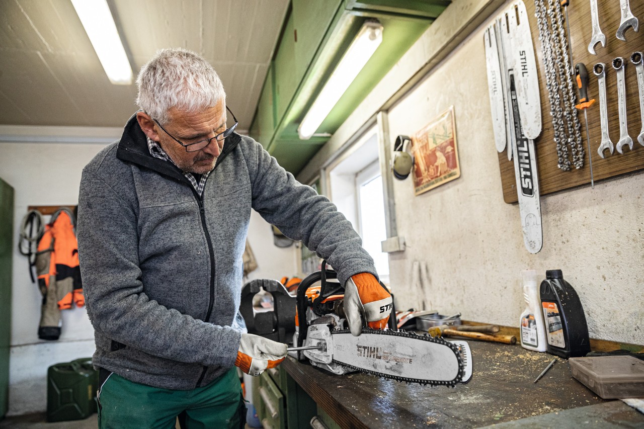En mand på et værksted skruer et STIHL Rollomatic E-sværd på en motorsav 