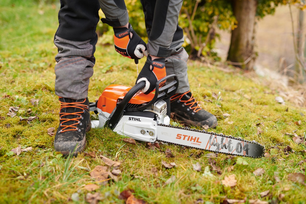 En person med handsker starter en STIHL MS 261 C-M benzinmotorsav med et Light 04-sværd