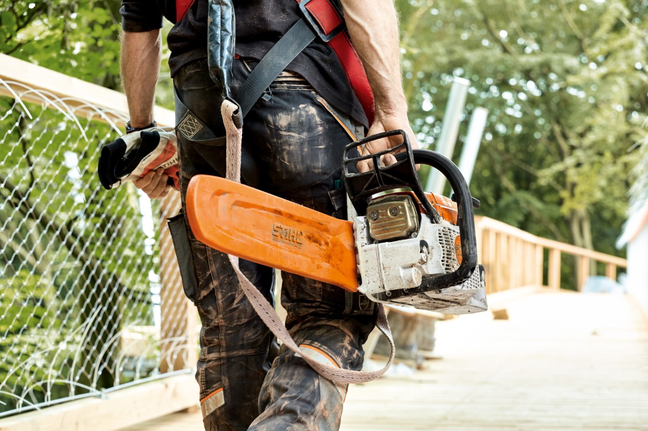 En STIHL MS 261-benzinmotorsav med kædeskærm bæres af en mand, der går over en bro
