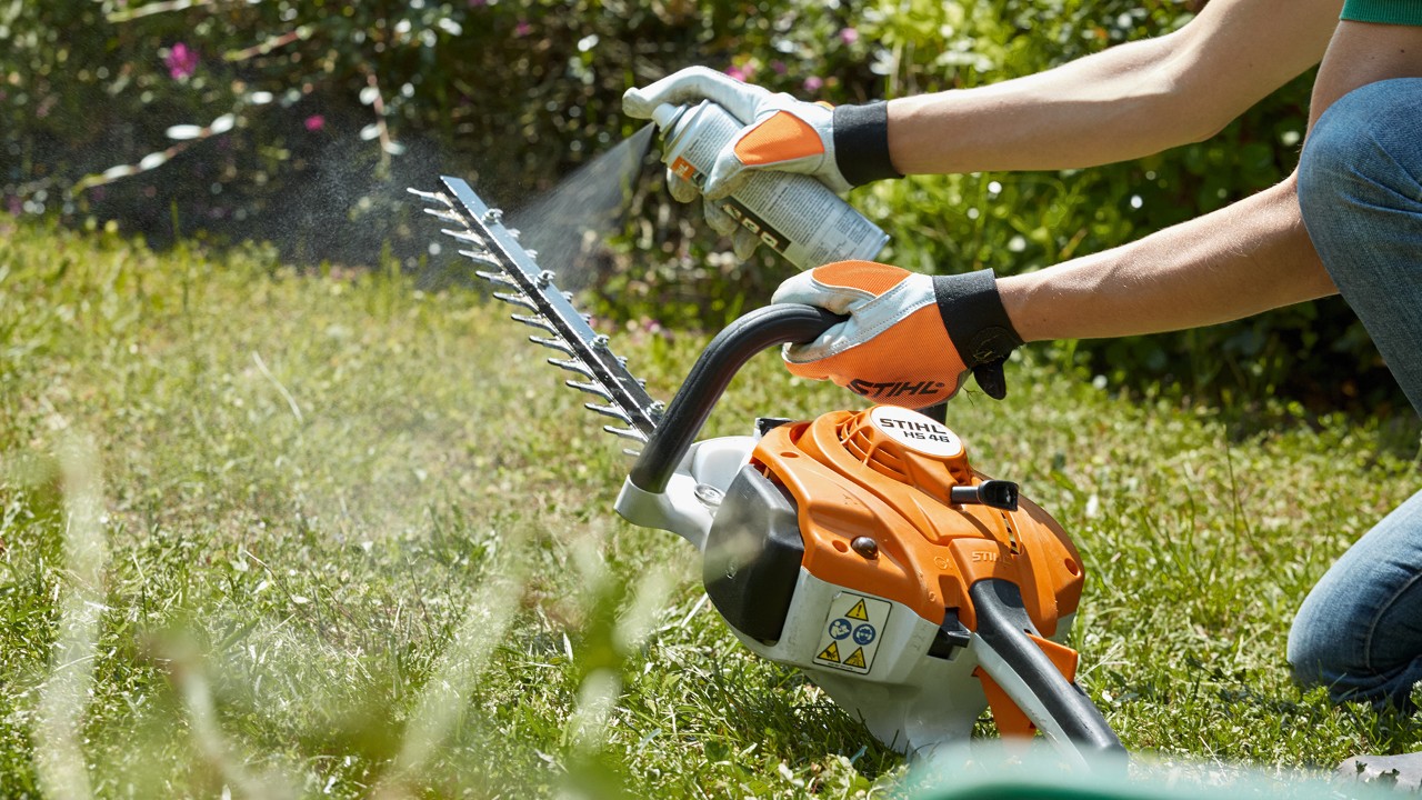 En STIHL HS 82 T benzindrevet hækkeklipper, der bliver sprøjtet ren på en grøn græsplæne