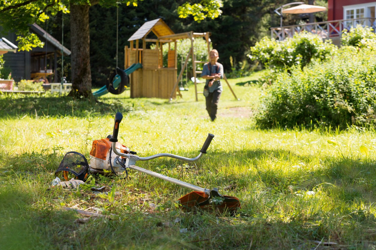 STIHL FS 240 buskrydder i græsset med en mand, der forbereder vedligeholdelse i baggrunden