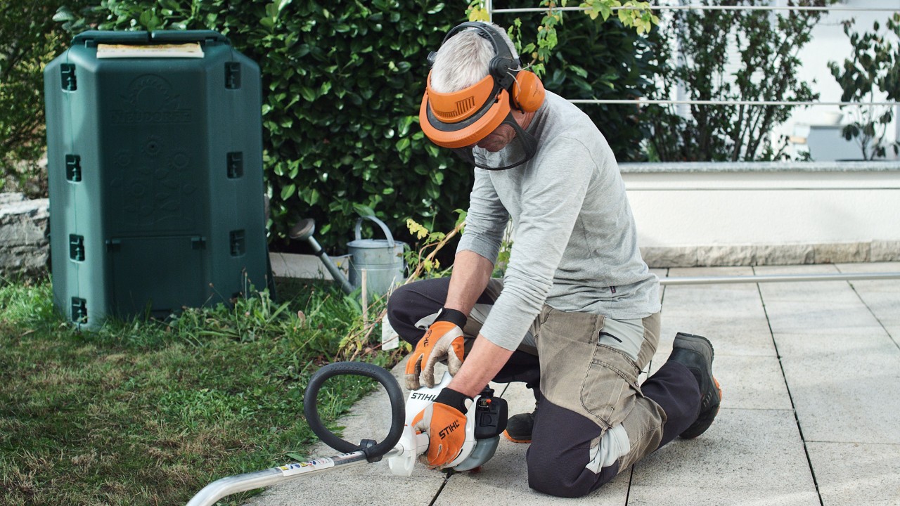En STIHL FS 38 benzindrevet buskrydder presses ned på jorden af en person iført beskyttelsesbekædning