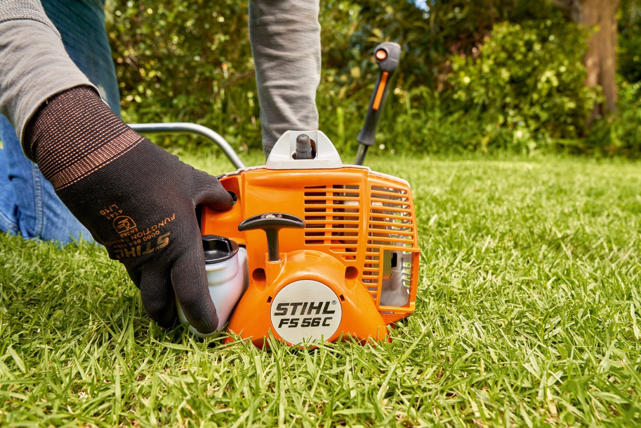 En mand trykker på brændstofpumpen på en STIHL FS 56 benzindrevet buskrydder for at starte den