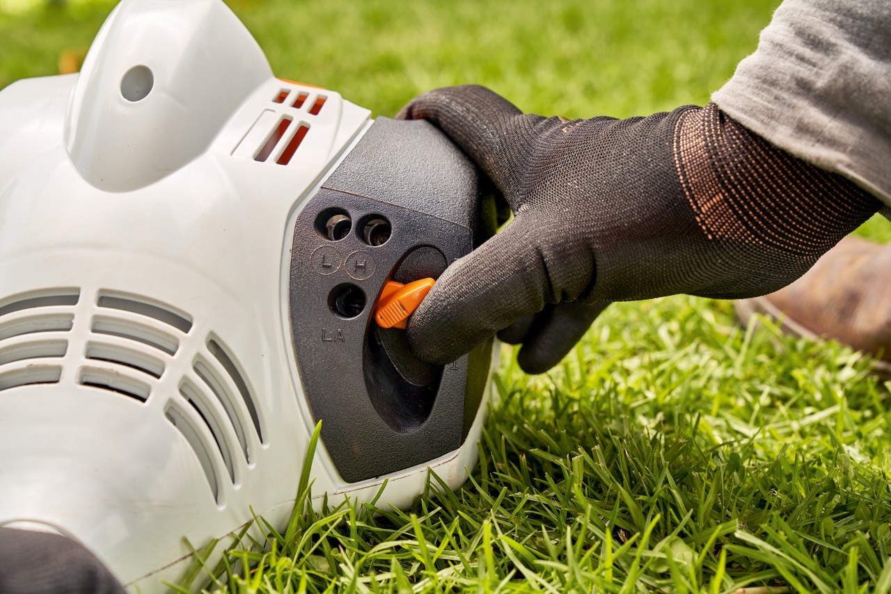 Mand, der justerer grebet på en STIHL FS 56 benzindrevet buskrydder for at starte den