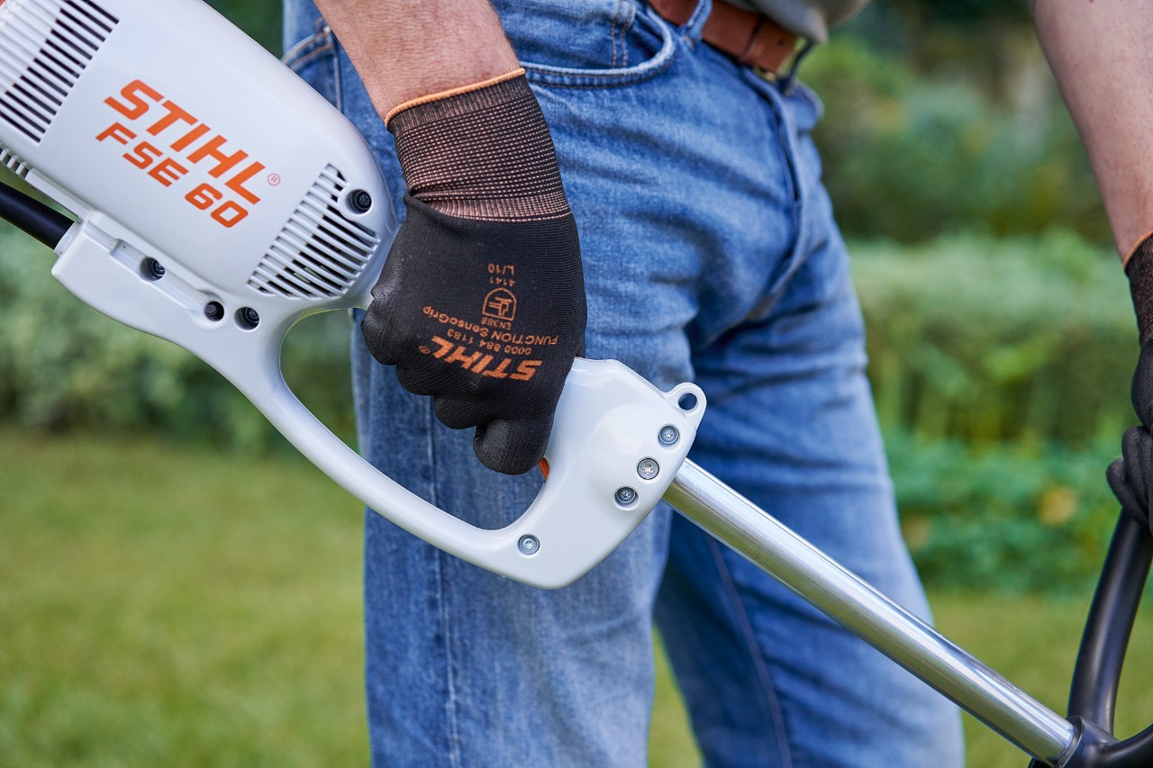Mand, der trykker på kontakten på betjeningshåndtaget på en elektrisk buskrydder STIHL FSE 60