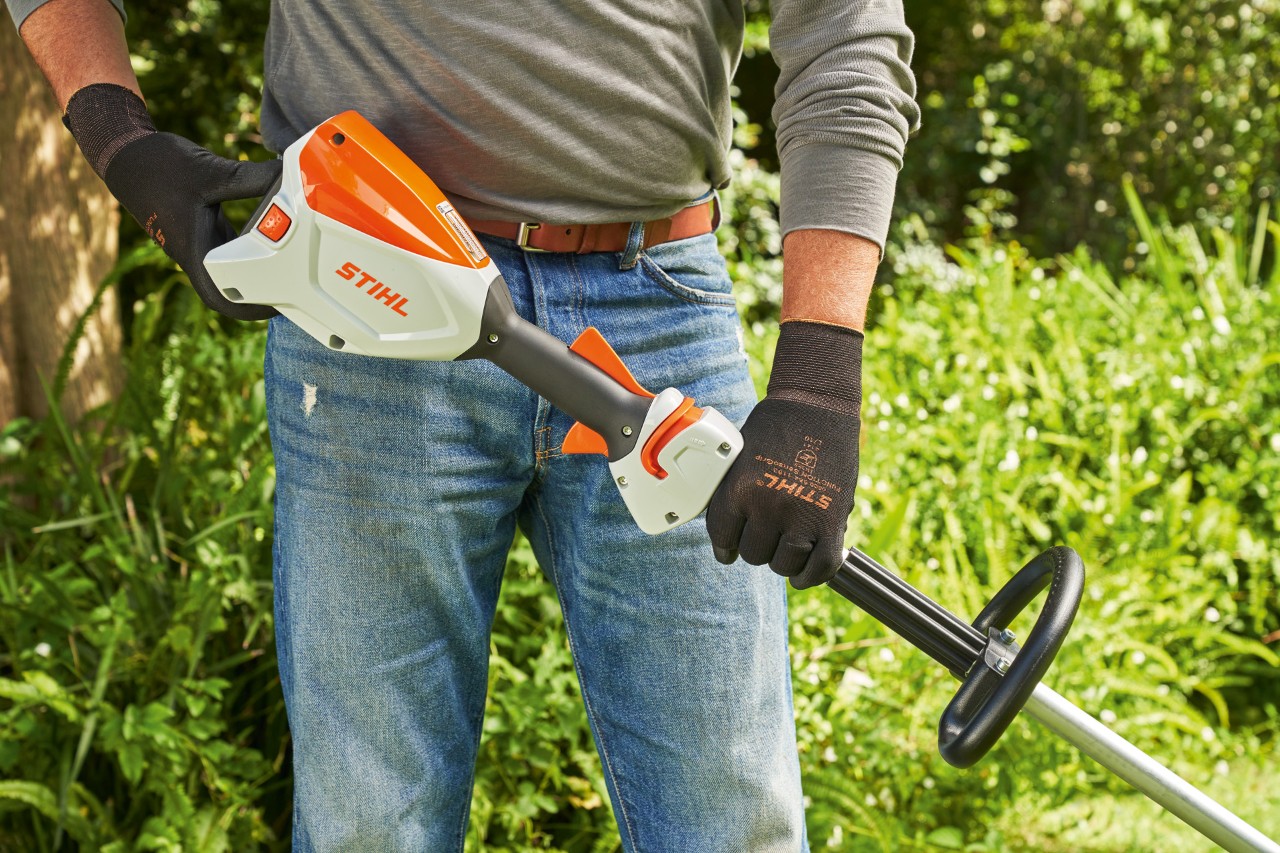 Mand med beskyttelseshandsker kontrollerer batteriet i den batteridrevne buskrydder STIHL FSA 60, før buskrydderen startes