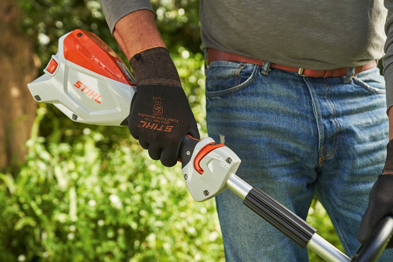 Mand med beskyttelseshandsker trykker på aftrækkeren på den batteridrevne buskrydder STIHL FSA 60 for at starte den