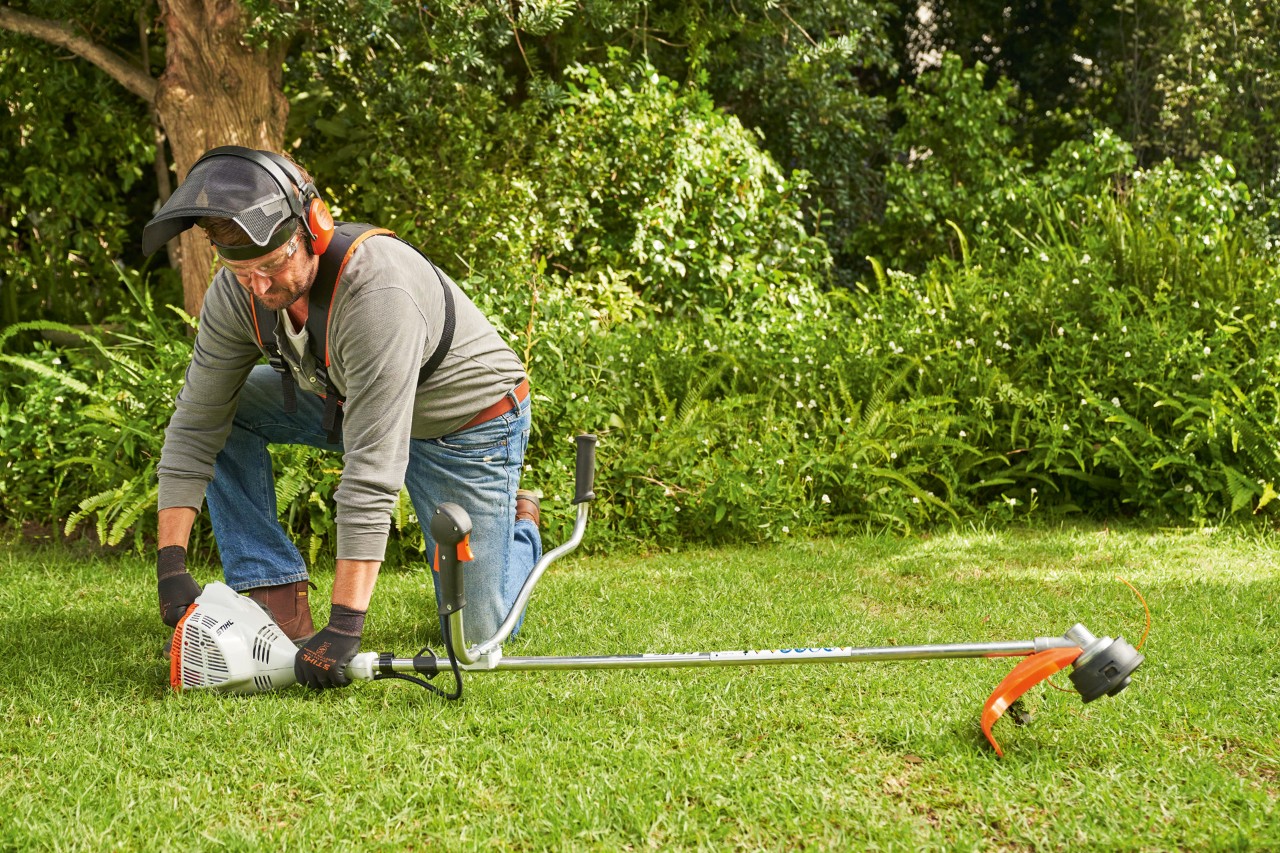 En mand med høreværn og ansigtsværn starter en STIHL FS 56 R benzindrevet buskrydder i en have