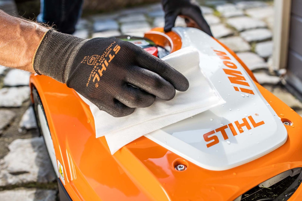 Nærbillede af toppen af en STIHL iMOW® robotplæneklipper, mens en person med handsker tørrer den af med en klud