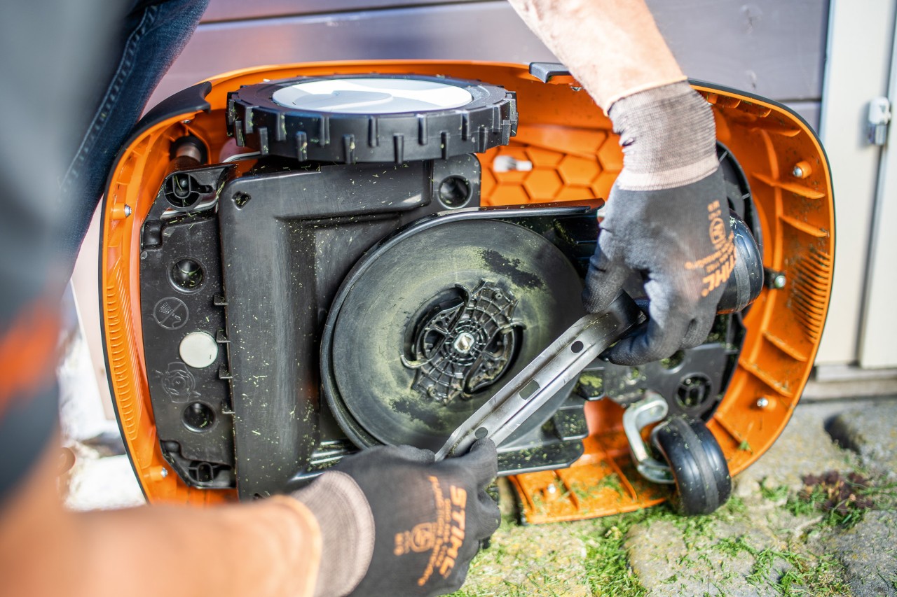En person inspicerer kniven på en STIHL iMOW® robotplæneklipper, mens den ligger på siden