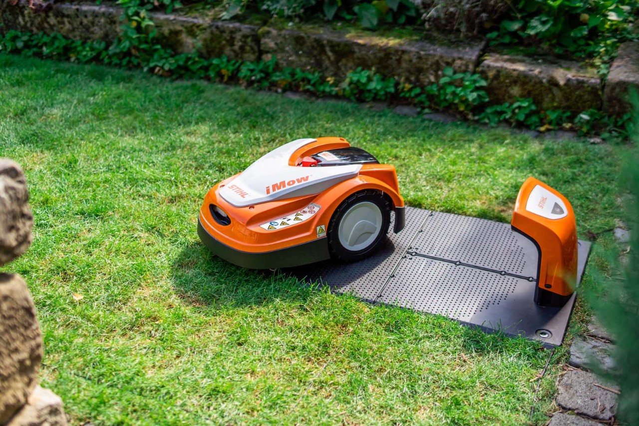 En STIHL iMOW® robotplæneklipper ved siden af sin dockingstation på en grøn græsplæne