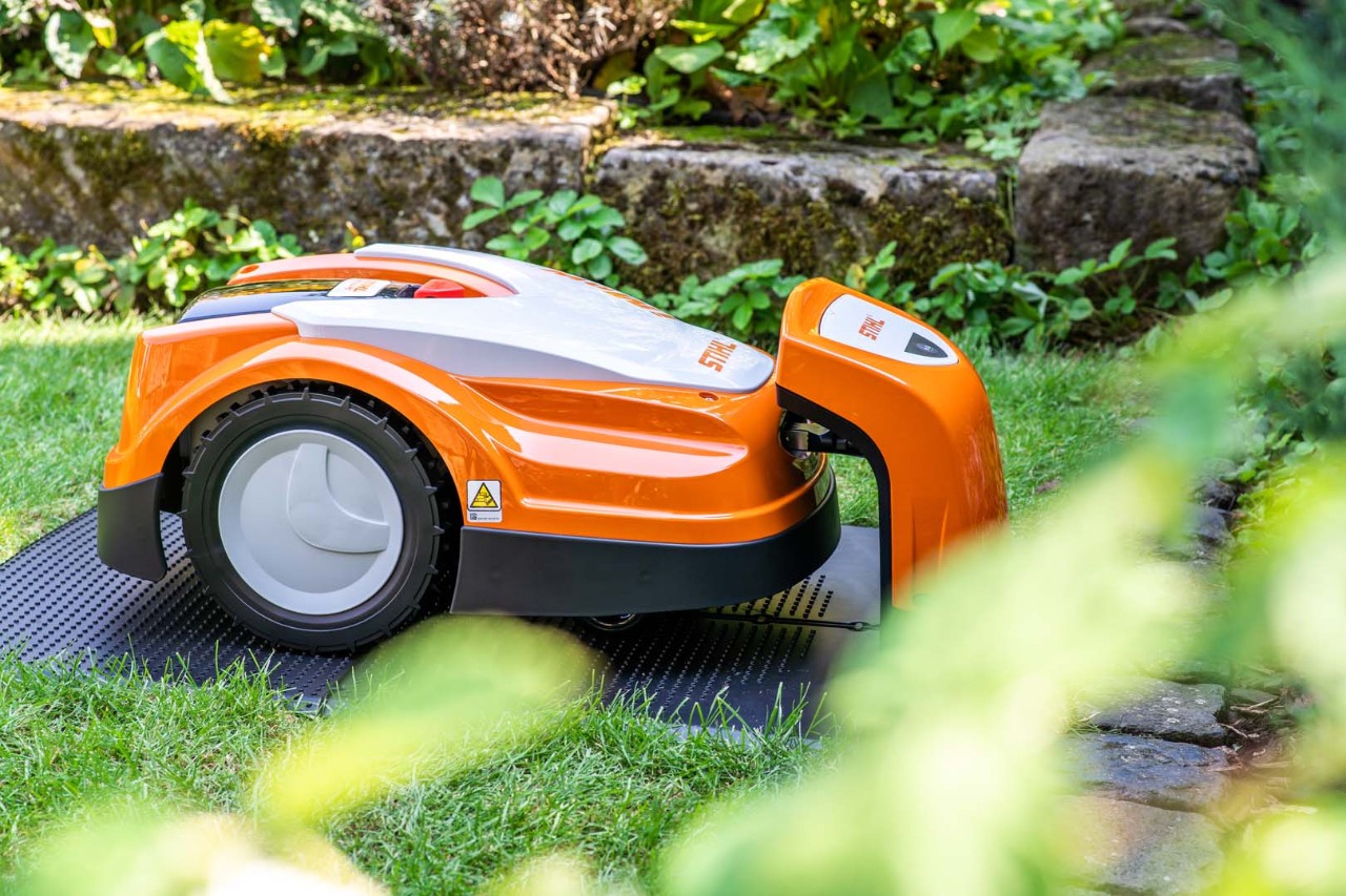 En STIHL iMOW® 422 robotplæneklipper i en have oplades i dockingstationen