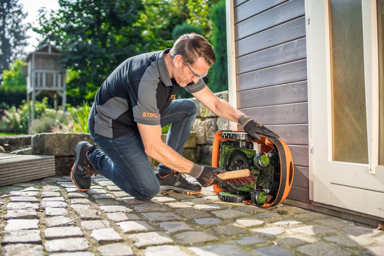 En mand bruger en børste til at rengøre undersiden af en STIHL iMOW® 422-robotplæneklipper. 
