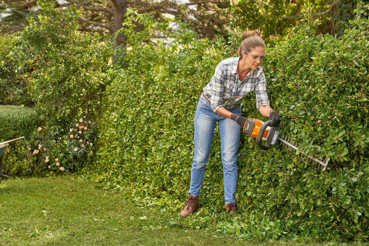 En kvinde anvender STIHL hækkeklipper HS 82 til at klippe en hæk