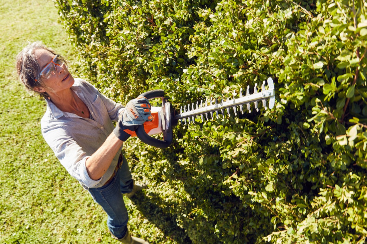 En kvinde med beskyttelsesbriller ved hækklipning med en STIHL batterihækkeklipper HSA 56