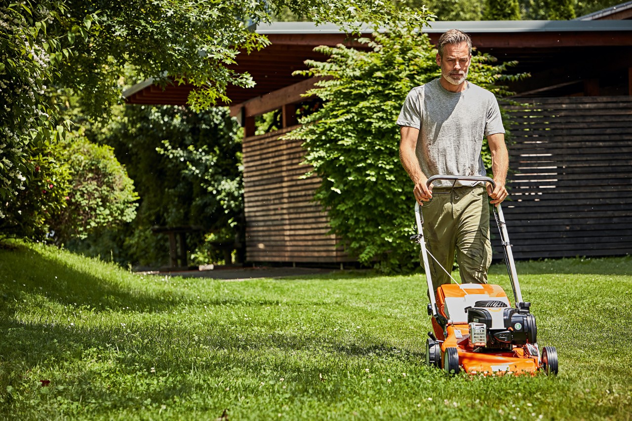 Plæneklippning på engen - en mand slår græsplænen med en STIHL plæneklipper.