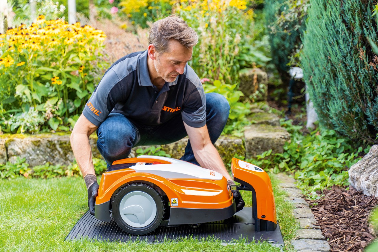 En STIHL-forhandler placerer en STIHL iMOW robotplæneklipper i sin ladestation i en have.