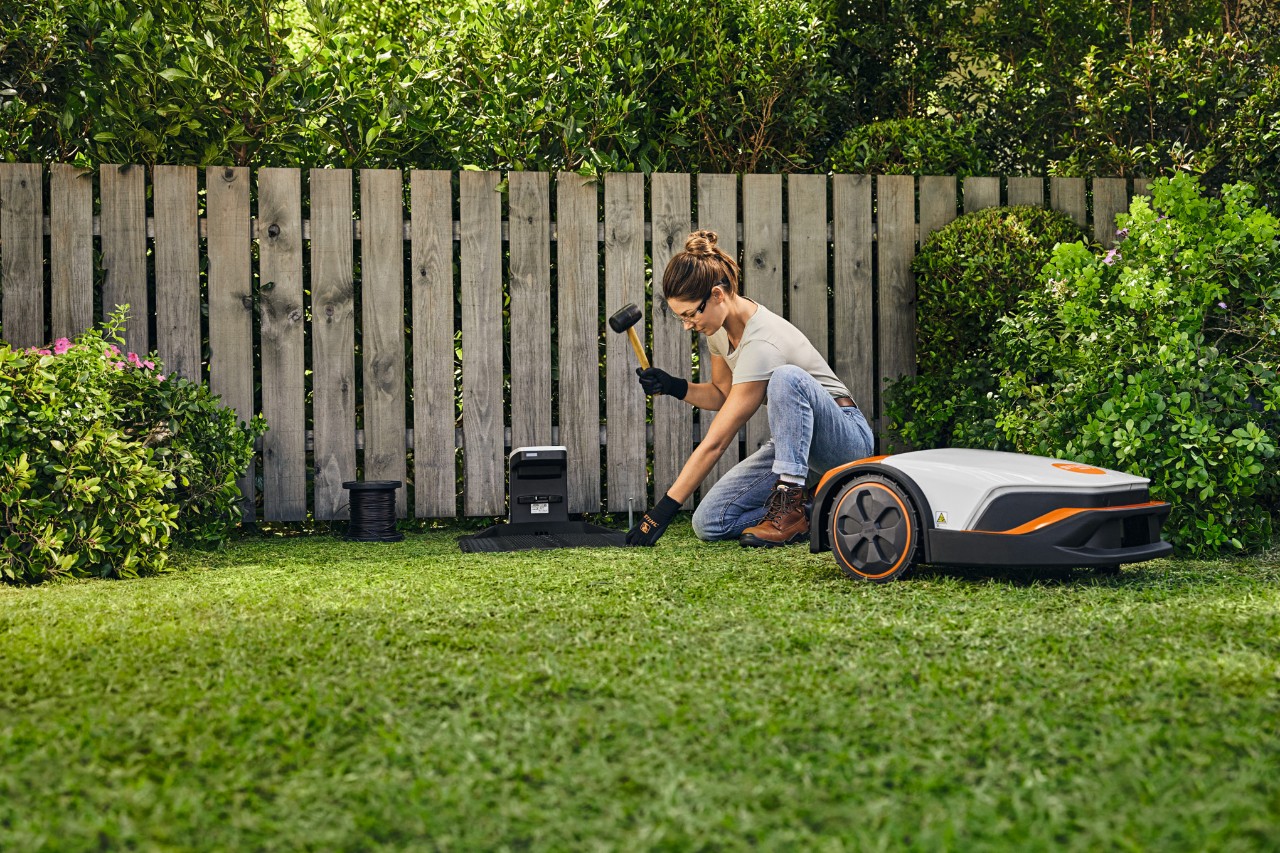 En kvinde installerer dockingstationen til sin STIHL iMOW® foran et hegn i sin have.