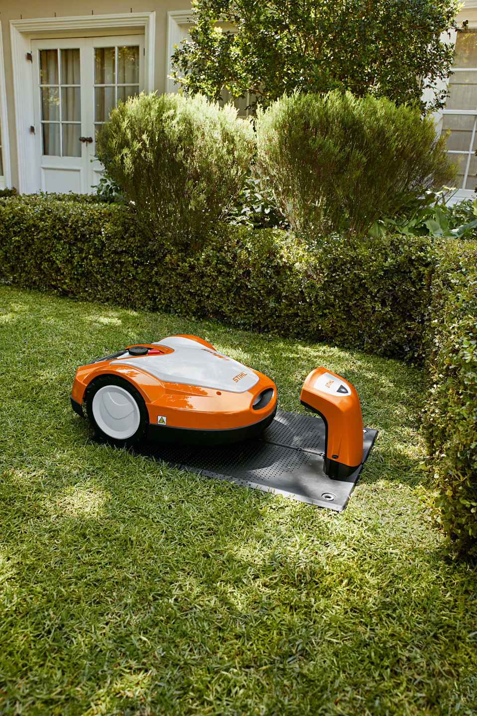 En STIHL iMOW® RMI 632 robotplæneklipper i sin ladestation i en have.